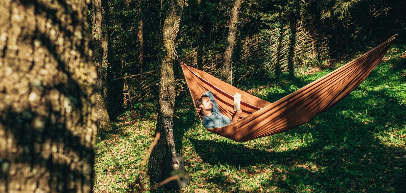 man in hammock reading book surrounded by green and brown trees