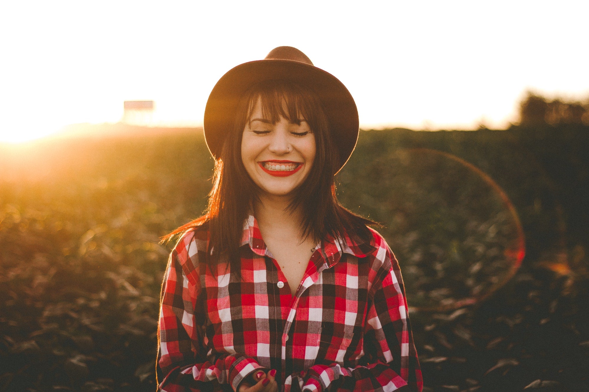 Woman in plaid shirt and hat, smiling with her eyes closed during golden hour