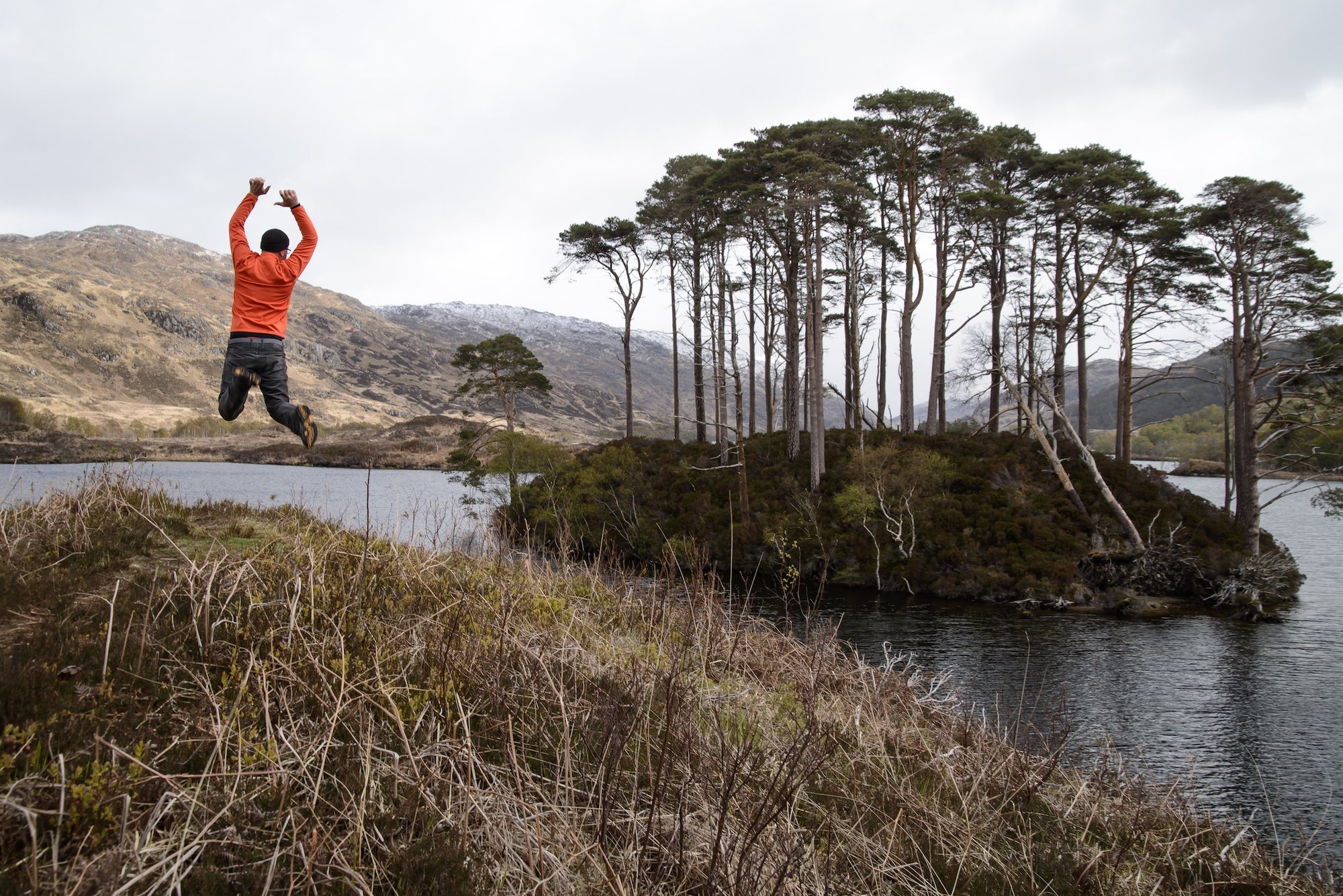 man jumping in the outdoors with trees and lake in background