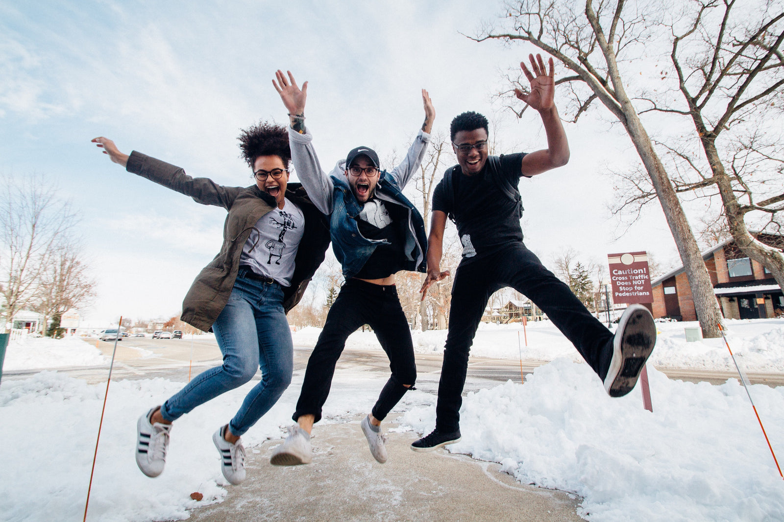 three people jumping in the snow in front of bare trees