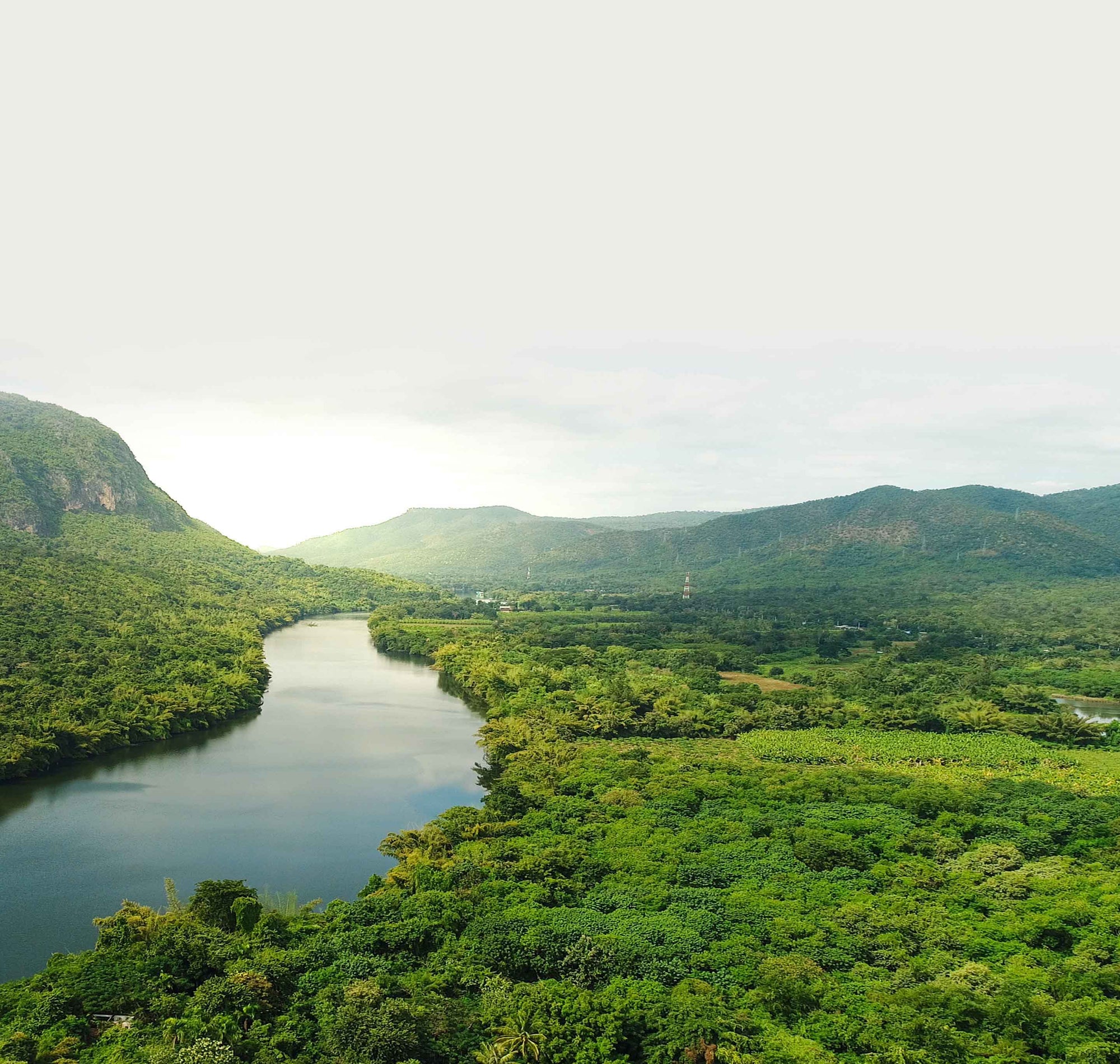 River surrounded by lush greenery and mountains under a cloudy sky