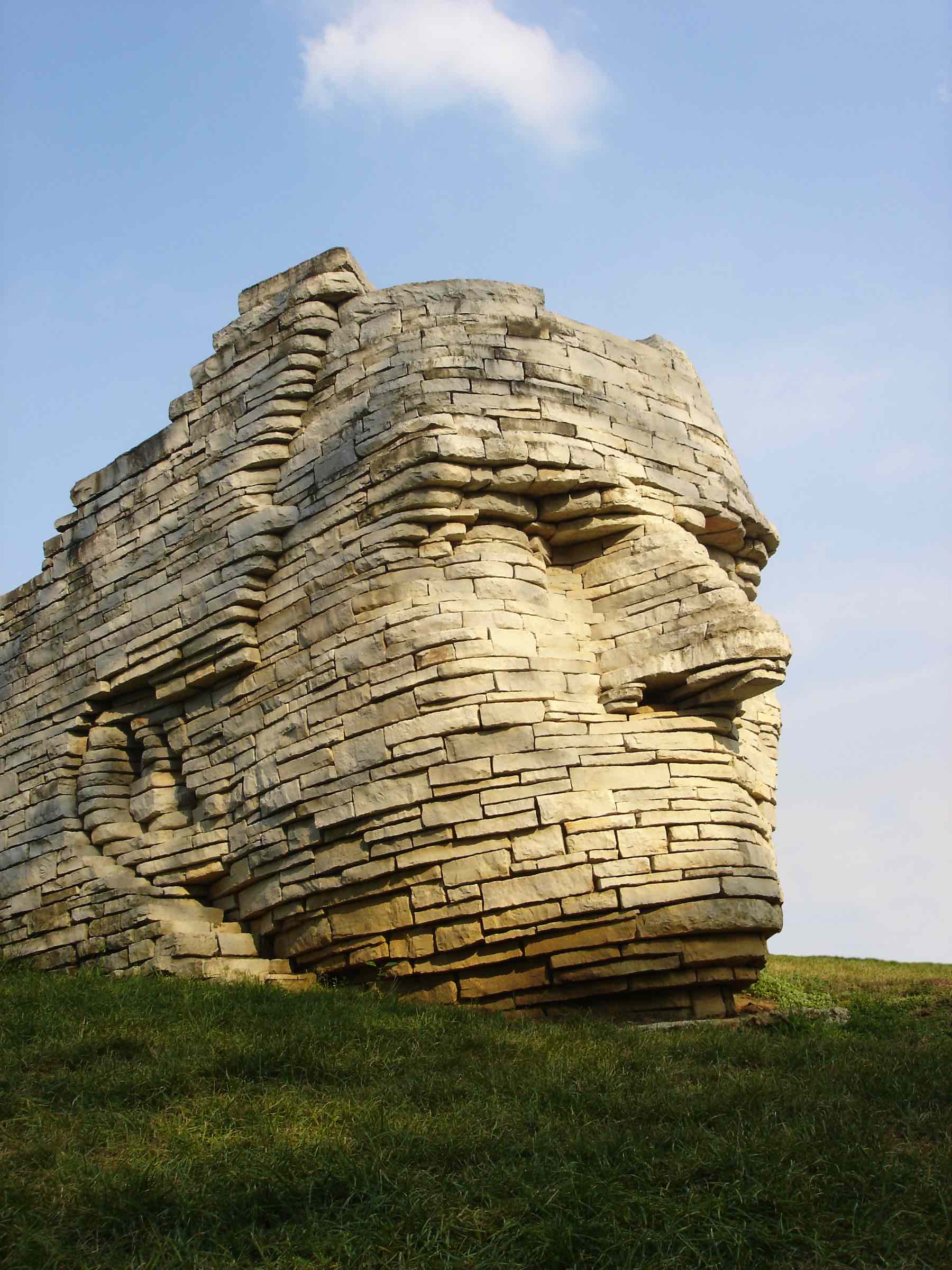 Large stone sculpture of a face on a grassy hill with a clear sky.