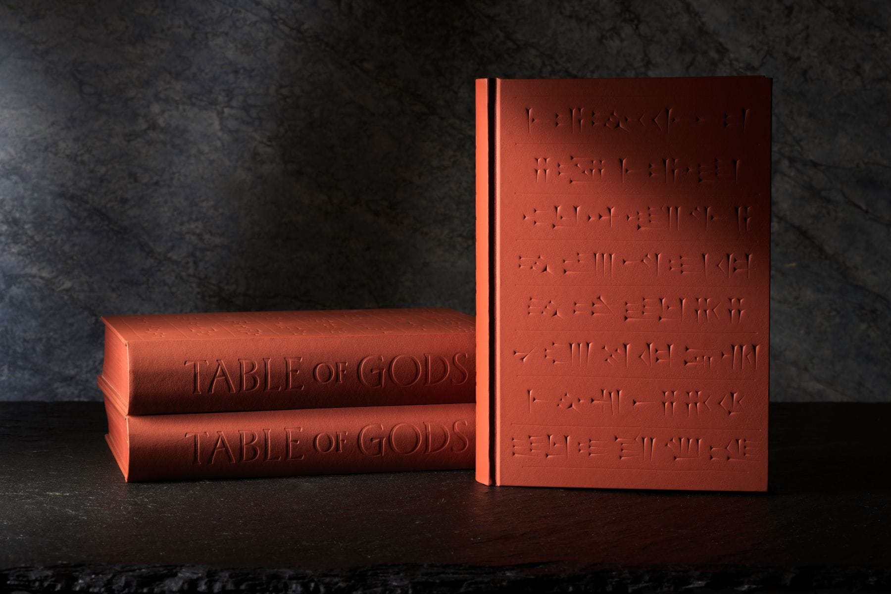image of three red clay colored cookbooks with cuneiform etched into the cover on dark gray stone counter
